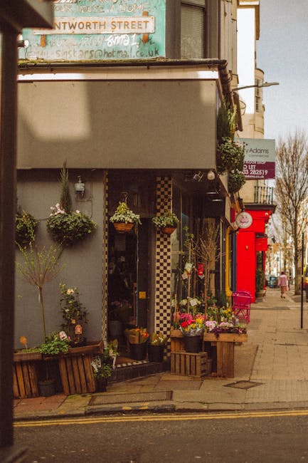 The image depicts the exterior of a florist shop on a street corner, featuring an inviting display of fresh flower bouquets and potted plants arranged outside the entrance. The floral arrangements sho