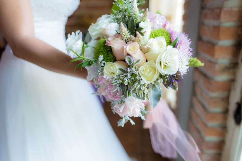 A bridal bouquet featuring a harmonious arrangement of fresh, cream-colored roses, soft pink hydrangeas, and delicate white lisianthus, accented with sprigs of greenery and variegated leaves. The bouq