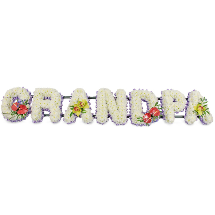 This image shows a carefully crafted funeral tribute spelling the word "GRANDPA" in large, sturdy capital letters, arranged horizontally as if resting on an easel or along the side of a coffin. Each letter is filled with tightly packed white chrysanthemums, their small, neat petals forming a dense blanket of flowers that communicates purity, peace and a sense of gentle softness. Around the base of every letter, a fine band of light lavender ribbon adds a discreet border, its cool lilac tone just visible through the edges of the petals, lending a subtle touch of colour and refinement without overpowering the white. The letters are linked together on dark green frames, giving a sense of depth and solid support while remaining mostly hidden behind the floral work. To personalise the tribute, four contrasting flower groupings break through the sea of white. On the left, the 'G' is dressed with a rich cluster of deep red anthuriums, their glossy, heart-shaped surfaces and bright yellow spadices surrounded by polished green leaves. Near the centre-right, the 'D' mirrors this arrangement with another spray of red anthuriums and foliage, creating visual balance. On the first 'A' and the final 'A', delicate yellow-green orchids with arching stems and star-like petals soften the structure, their light, fresh colour adding an air of hope and remembrance. The overall composition feels calm and dignified, the sort of bespoke "GRANDPA" lettering a family in Hatch End might order for a funeral at a local church or crematorium, reflecting love, gratitude and respect for a cherished grandfather through skilled, thoughtful floristry.